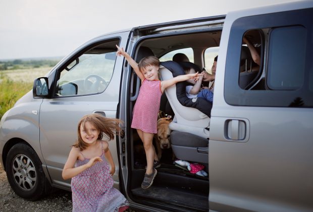 Children with a dog in a big car minivan stopover on a road trip. Concept family travel with children and animals, local travel